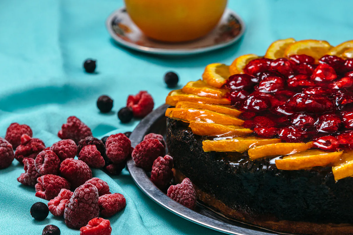 Gyümölcsökkel díszített torta türkiz háttér előtt.